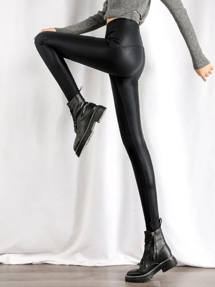 Des leggings ou des pantalons moulants noirs brillants portés avec des bottines et un haut gris.
